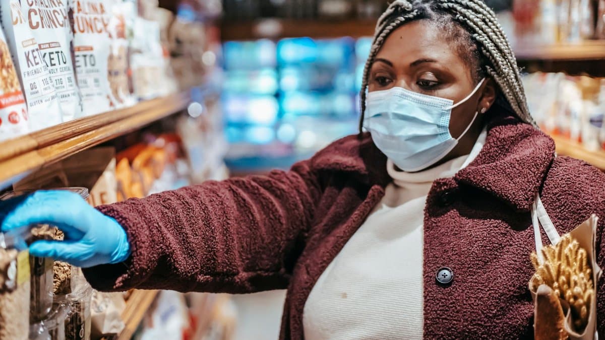 African American female buyer in protective mask picking food from shelf in grocery store