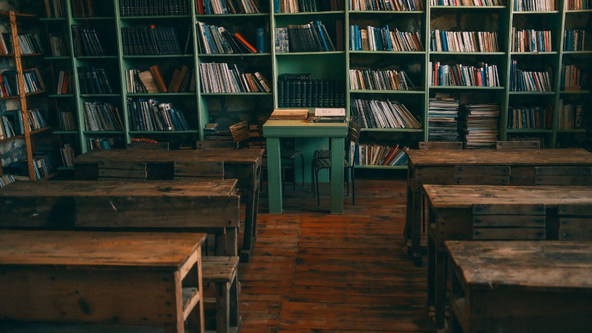 A nostalgic view of an old classroom with wooden desks and bookshelves filled with books.