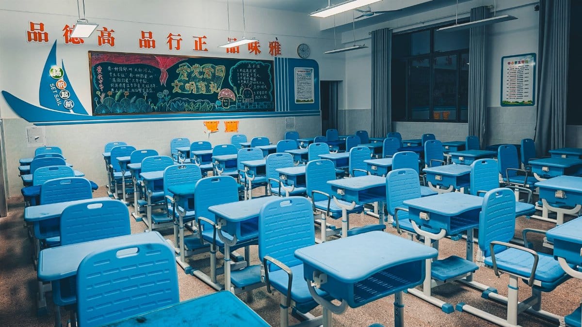 Spacious classroom with blue desks and vibrant decorated chalkboard, ready for students.