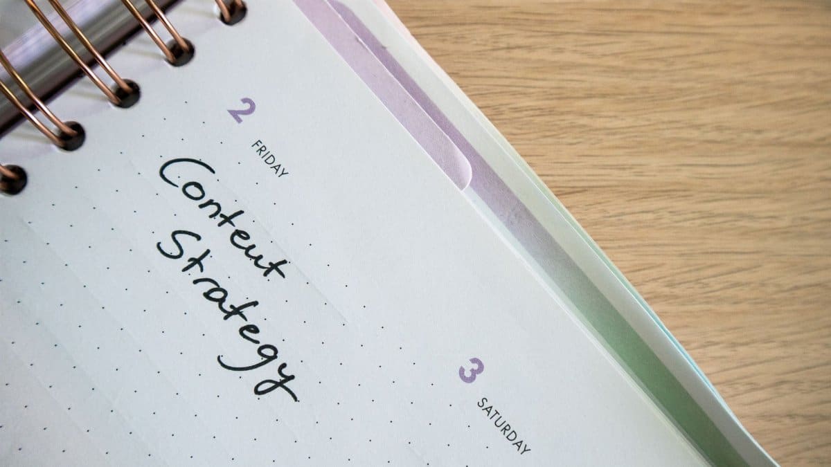 Top view of a notebook open to a day planner featuring 'Content Strategy' handwritten, lying on a wooden desk.