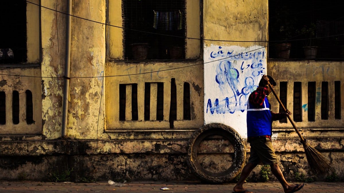 A man cleaning a graffiti-covered wall beside a worn building, capturing urban life.
