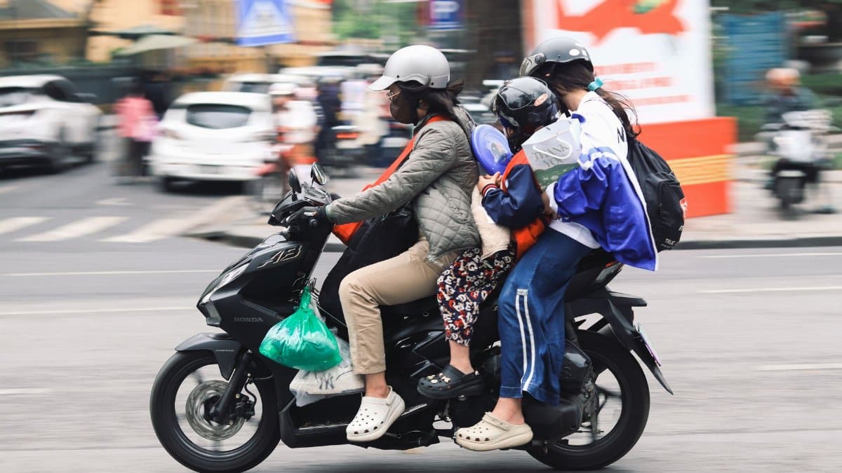 A family of four travels on a motorbike down a lively urban street, demonstrating local transportation methods.