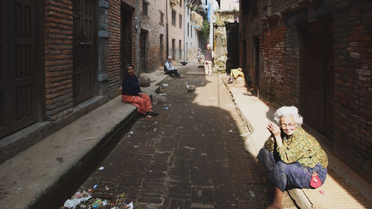 A narrow alleyway in a historical town with senior residents sitting and enjoying the sunny day.