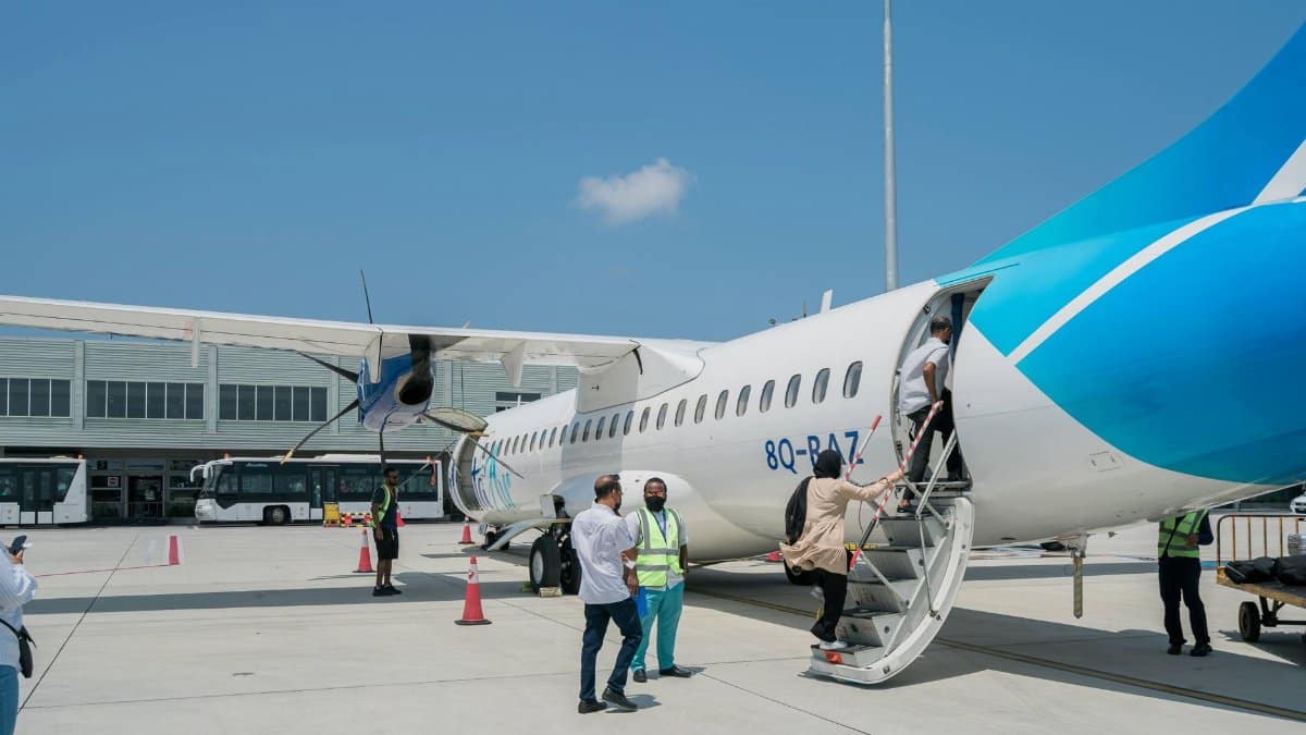 Passengers board a blue and white ATR 72 aircraft at an airport under clear skies.