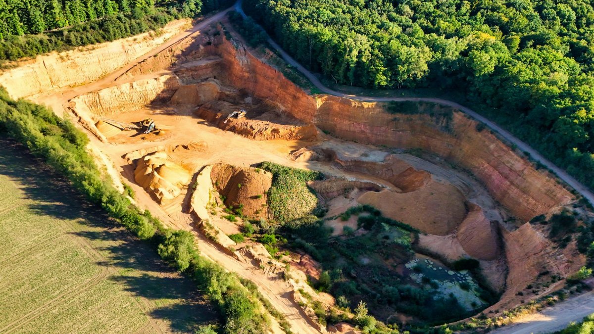 A stunning aerial shot of a large quarry contrasting sharply with lush green forests.