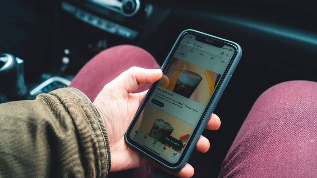 Hand holding smartphone showing a coffee app interface in a car interior setting.