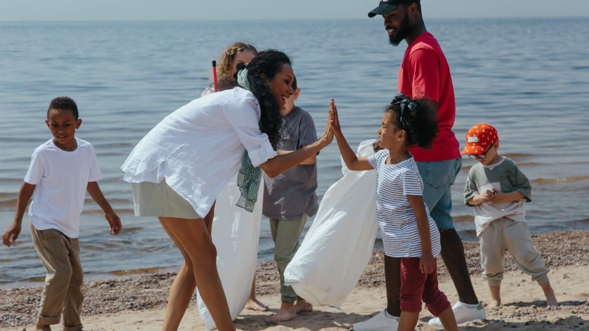 A diverse group of volunteers, including children and adults, clean up a beach and celebrate with high-fives.