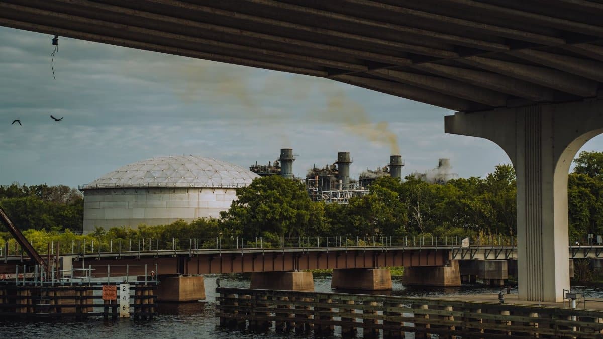 Industrial plant emitting smoke under a bridge in Sanford, Florida. Environmental impact depicted.
