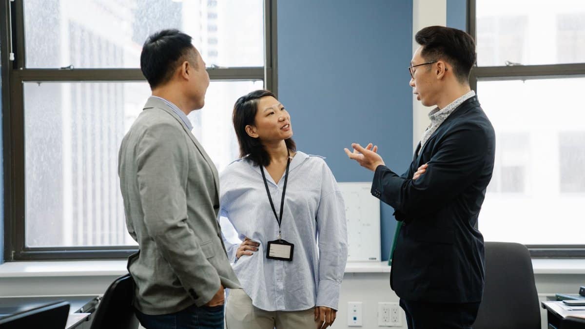 Three professional adults engaged in a lively discussion in a contemporary office environment.