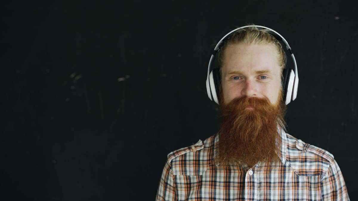 Stylish bearded man wearing headphones against black background.