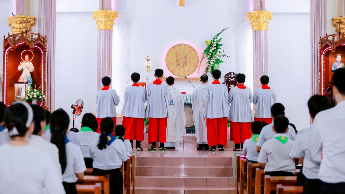 Catholic mass with altar servers and congregation inside a church.