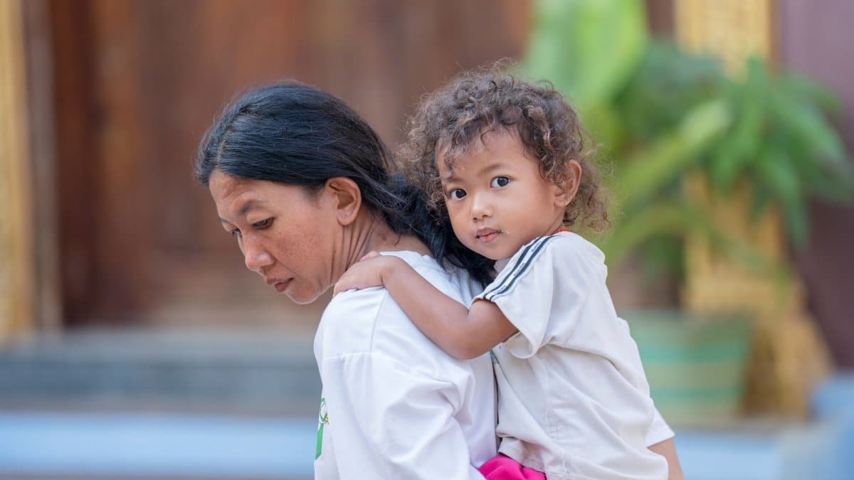 A mother carrying her child outdoors in Battambang, Cambodia, showcasing family bonds.