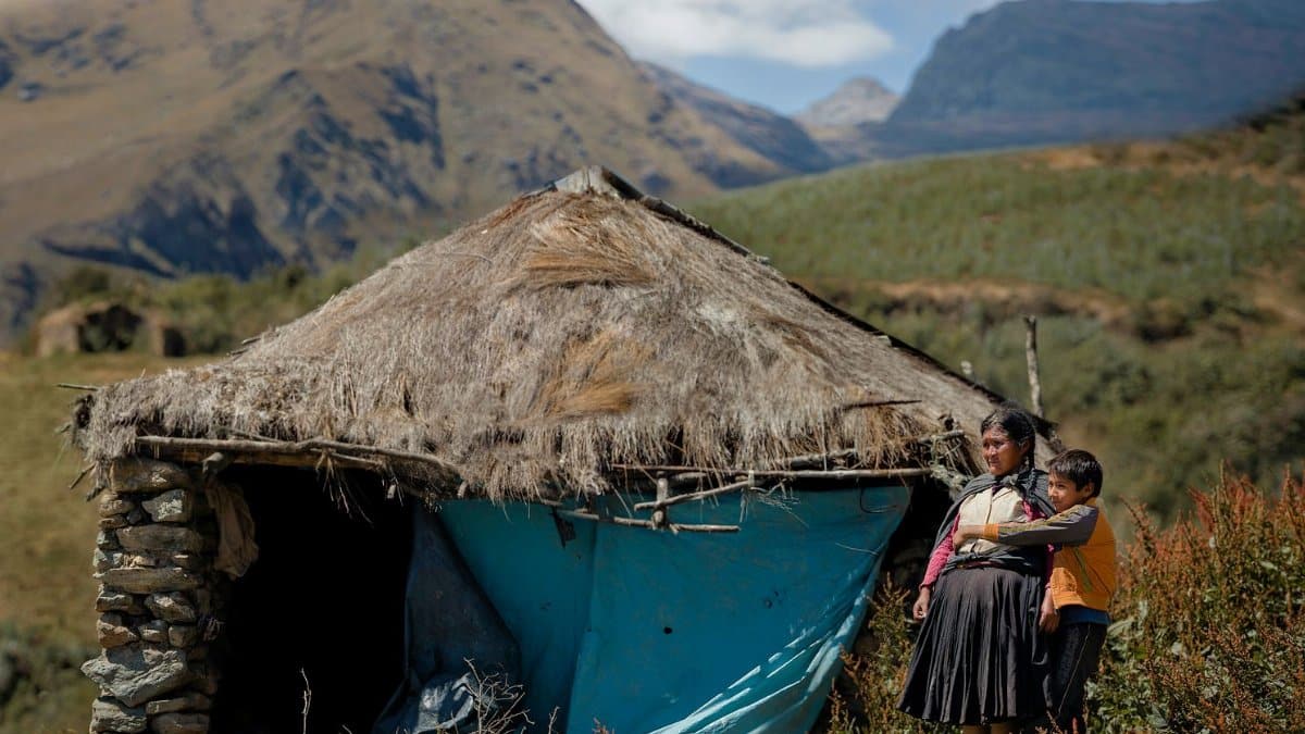 A woman and child stand by a traditional hut in the Andean mountains of Huánuco, Peru, showcasing local culture.