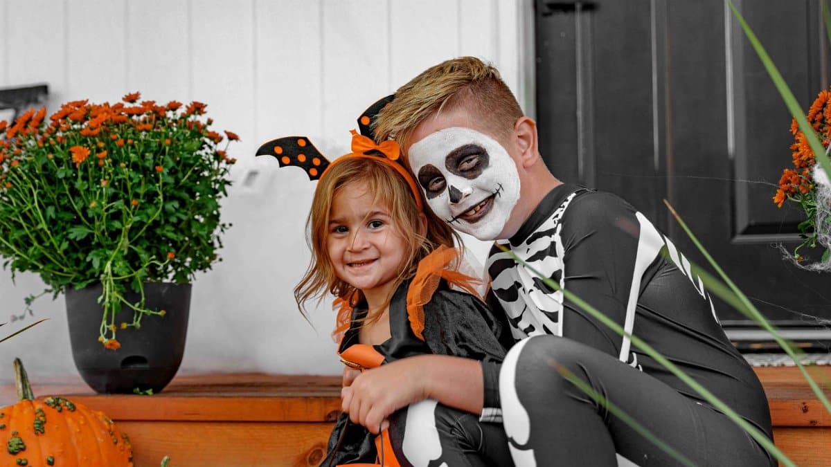 Kids in Halloween costumes posed with pumpkins on a decorated porch.