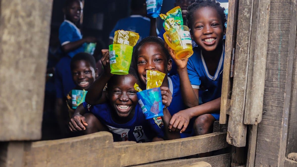 Children smiling and holding colorful recycled plastic cups in a school setting.