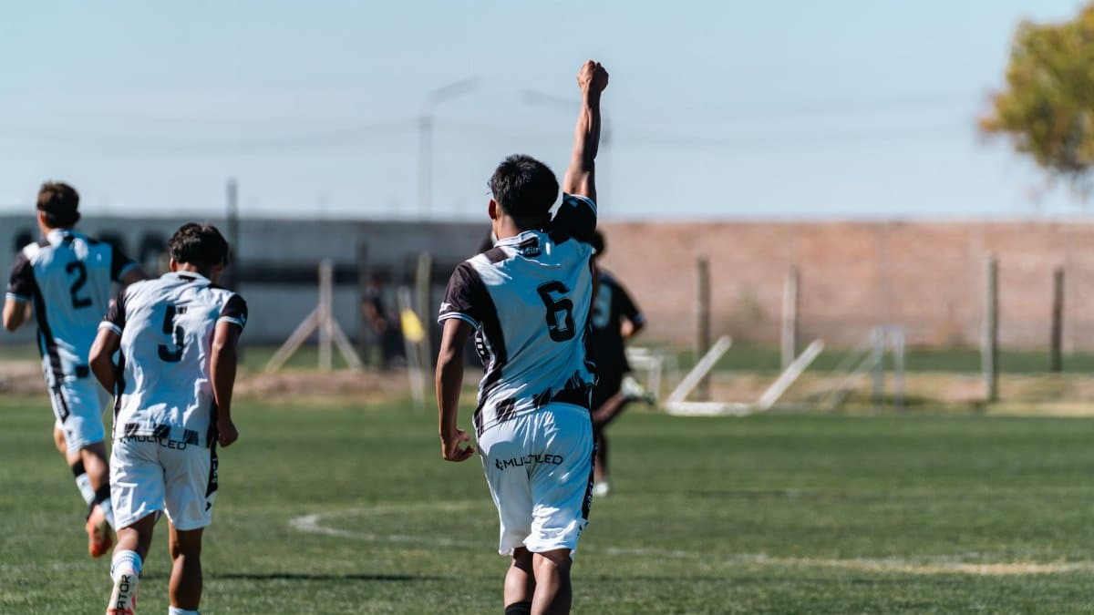 Youth soccer players celebrate a goal on a bright outdoor field.
