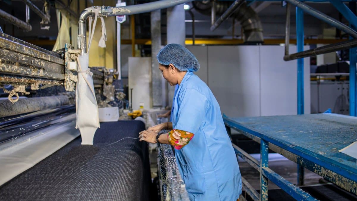 A female textile worker operates machinery in a factory, showcasing industrial production.