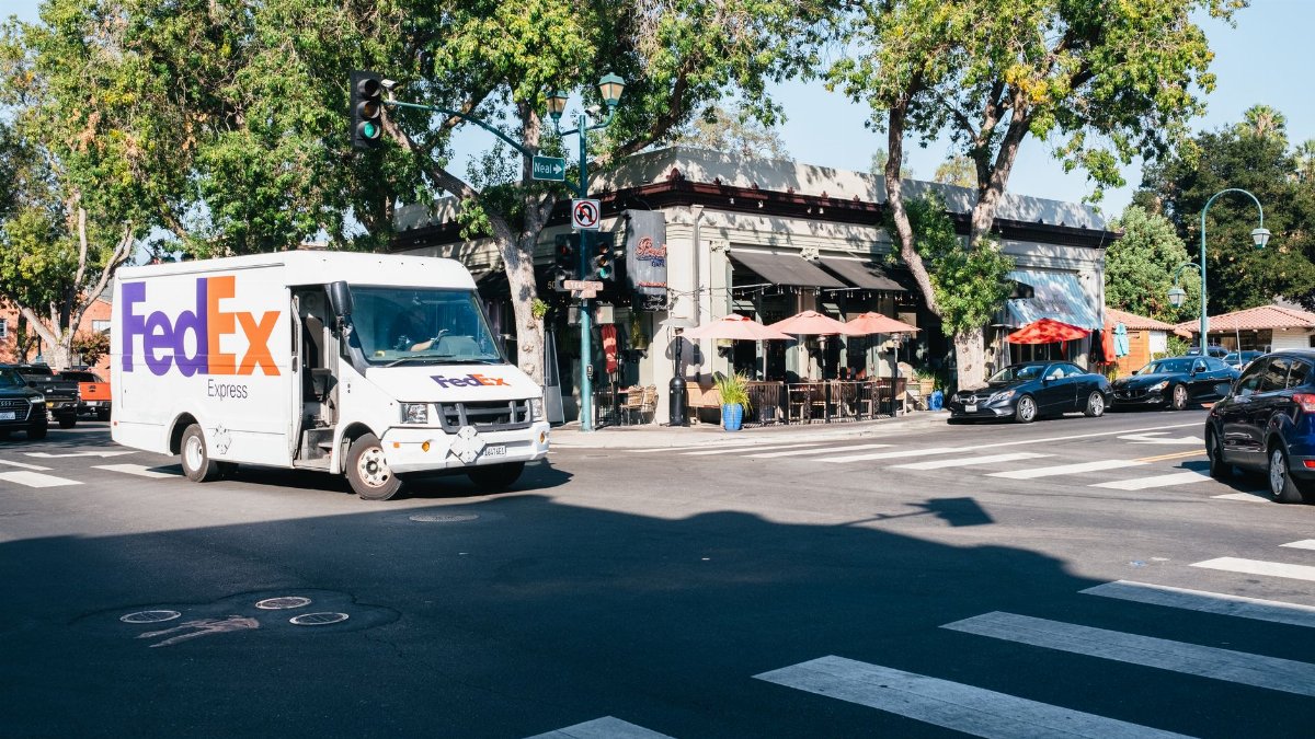 FedEx van navigating a lively city intersection with bustling traffic and restaurants nearby.