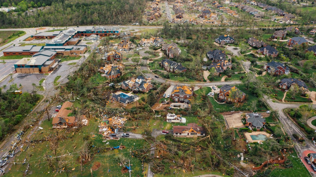 Aerial view of tornado impact on small settlement cottages with destroyed roofs windthrown trees and bent electricity transmission lines