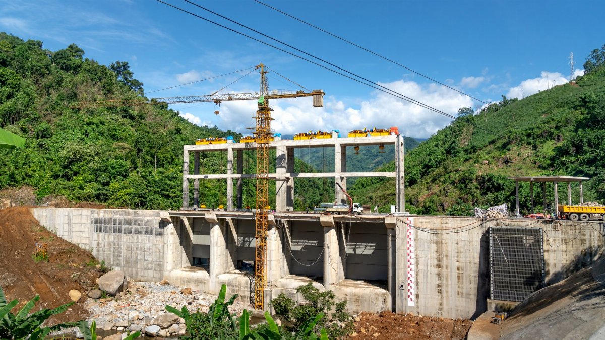 Crane operating at a construction site in a lush, mountainous area under bright blue skies.