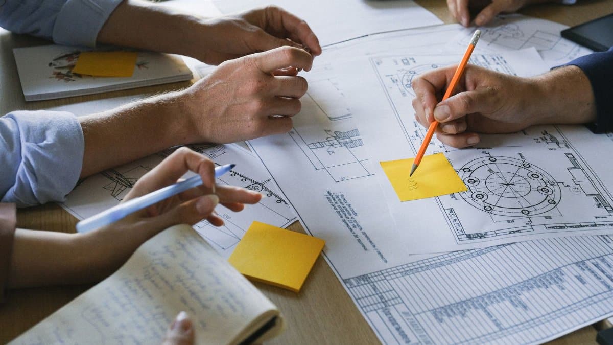 Crop anonymous coworkers sitting at table with documents and discussing project during brainstorm in light office in daytime