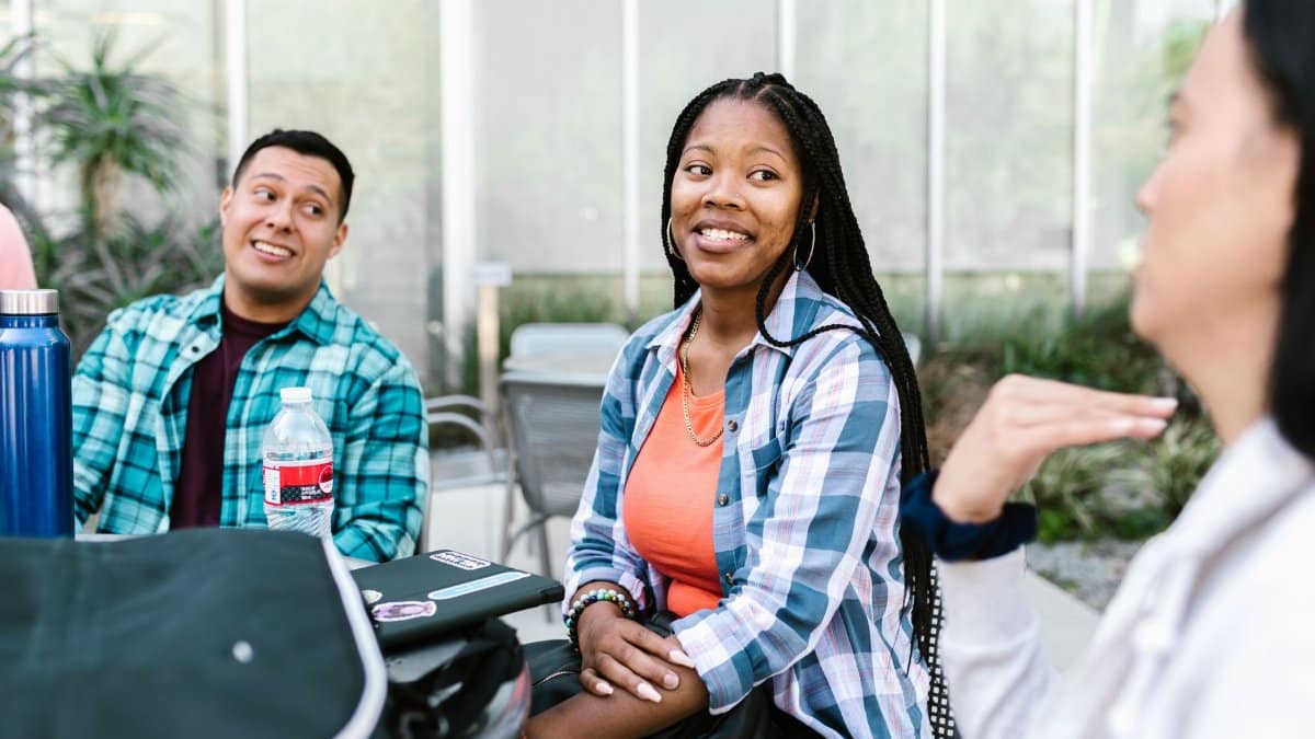 A group of diverse college students having a conversation outside in a relaxed campus setting.
