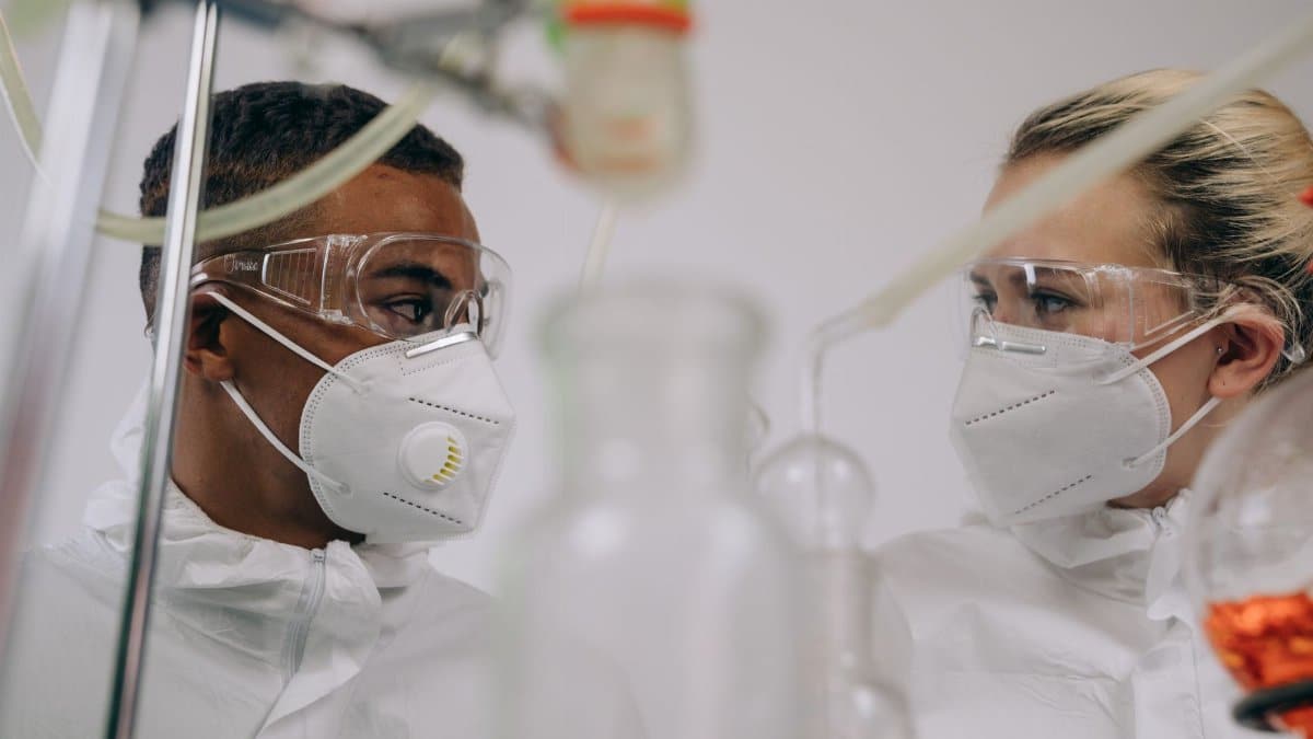 Two scientists in protective suits and masks working in a laboratory setting with equipment.