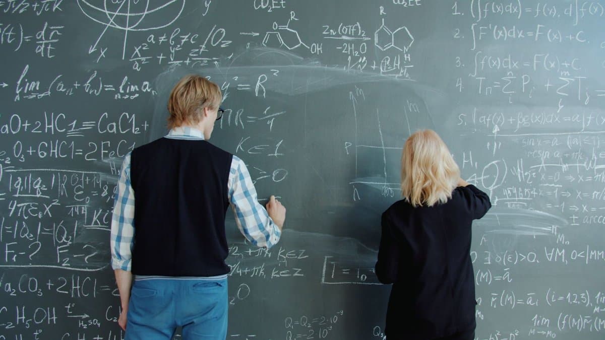 Two students solving complex math and chemistry equations on a chalkboard.