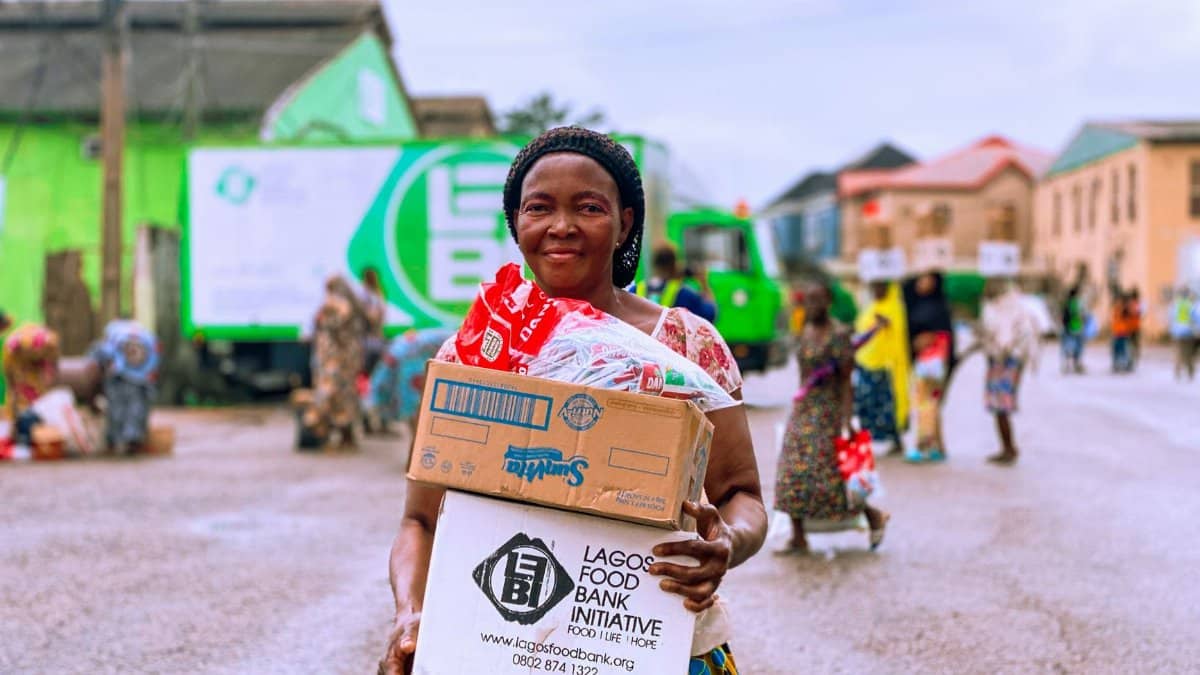 Smiling woman holding a food box from Lagos Food Bank on a busy street in Lagos, Nigeria.