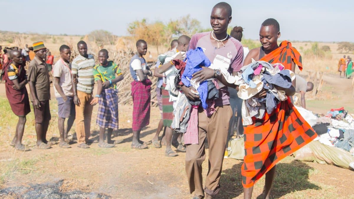 Local community members participate in a clothing distribution event under sunny skies in a rural setting.