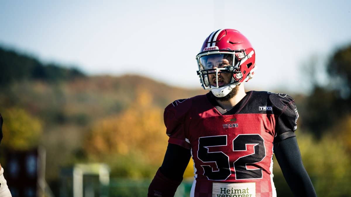 Male American football player in red uniform and helmet captured mid-game outdoors in daytime.