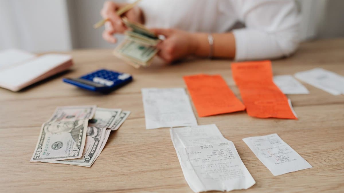A person using a calculator and cash to plan a household budget.