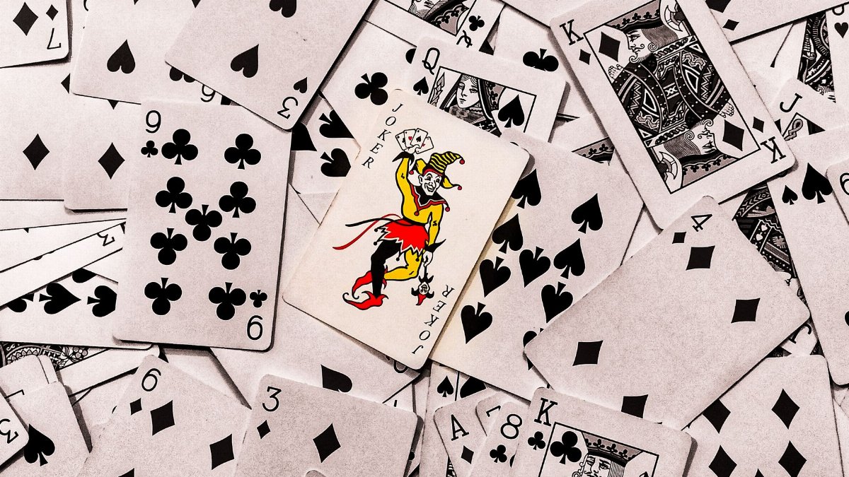 A vibrant joker card stands out in a scattered deck of monochrome playing cards.