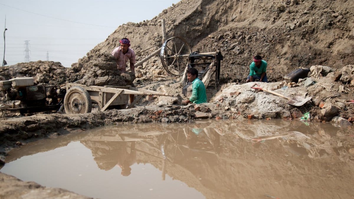 Workers laboring in muddy conditions at a mine in Gabtoli, Bangladesh, illustrating harsh labor challenges.