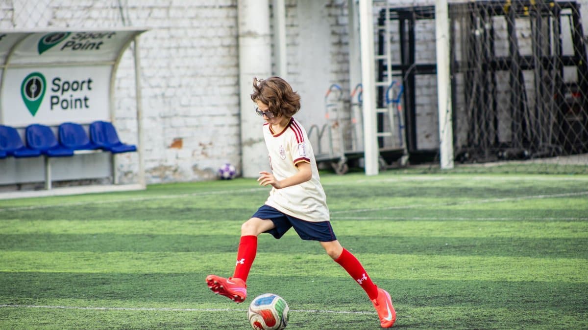 Young boy playing soccer on a sports field, wearing red socks and focused on the game.