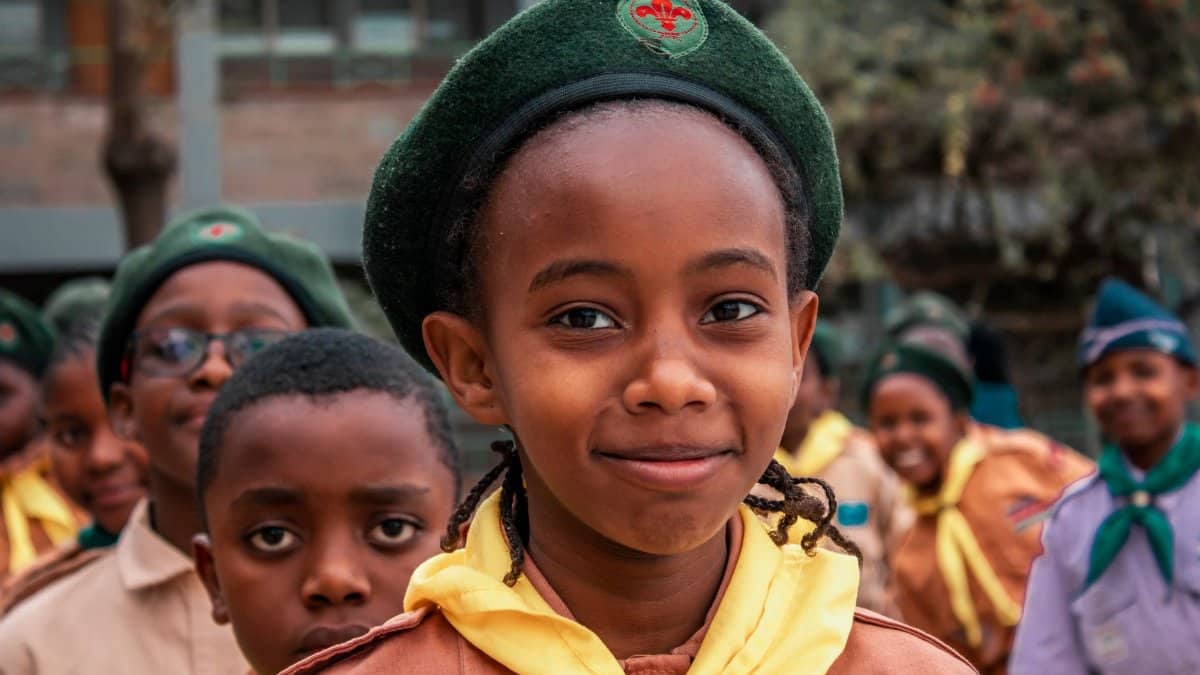 A smiling girl scout in uniform with her friends standing outdoors, ready for adventure.