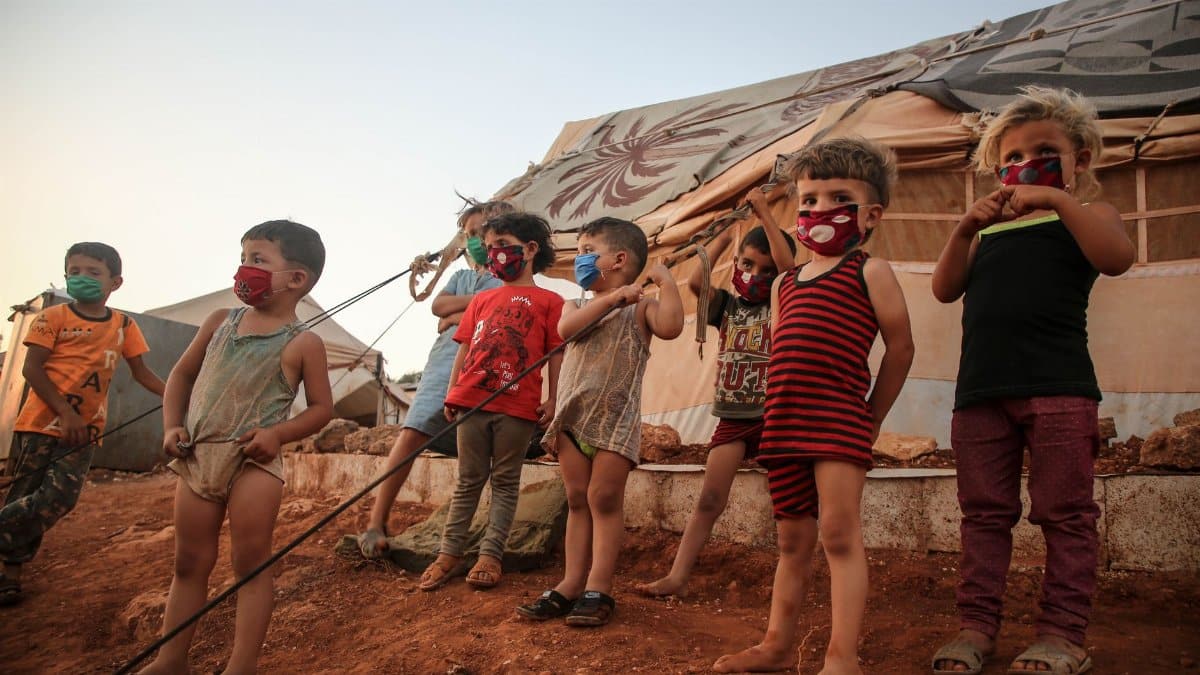 Young children wearing masks in a Syrian refugee camp, highlighting the impact of the pandemic.