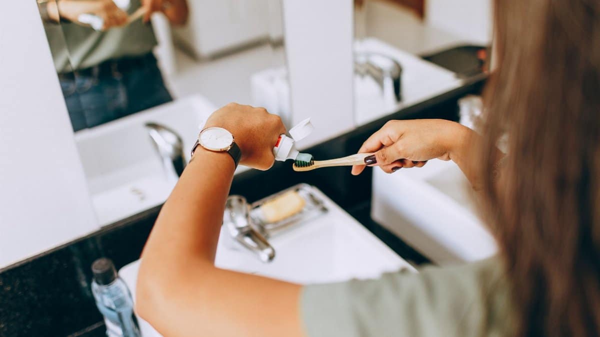A woman is applying toothpaste to a toothbrush in a bathroom setting, showing daily oral hygiene habits.