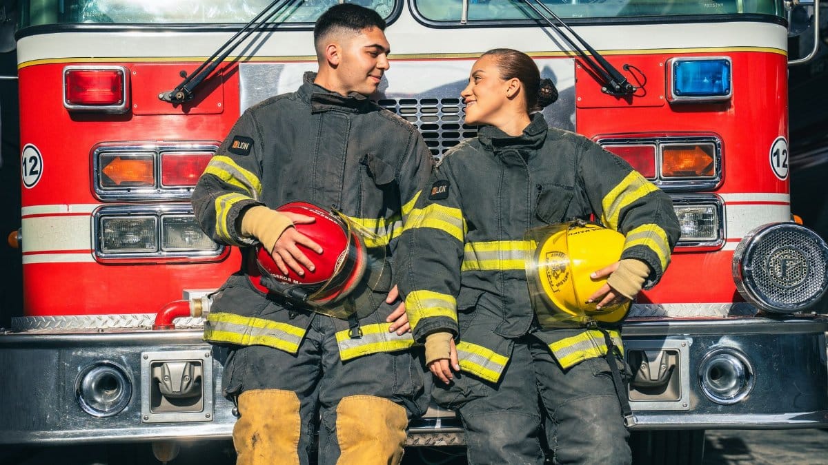 Two firefighters smiling while sitting in front of a fire truck.