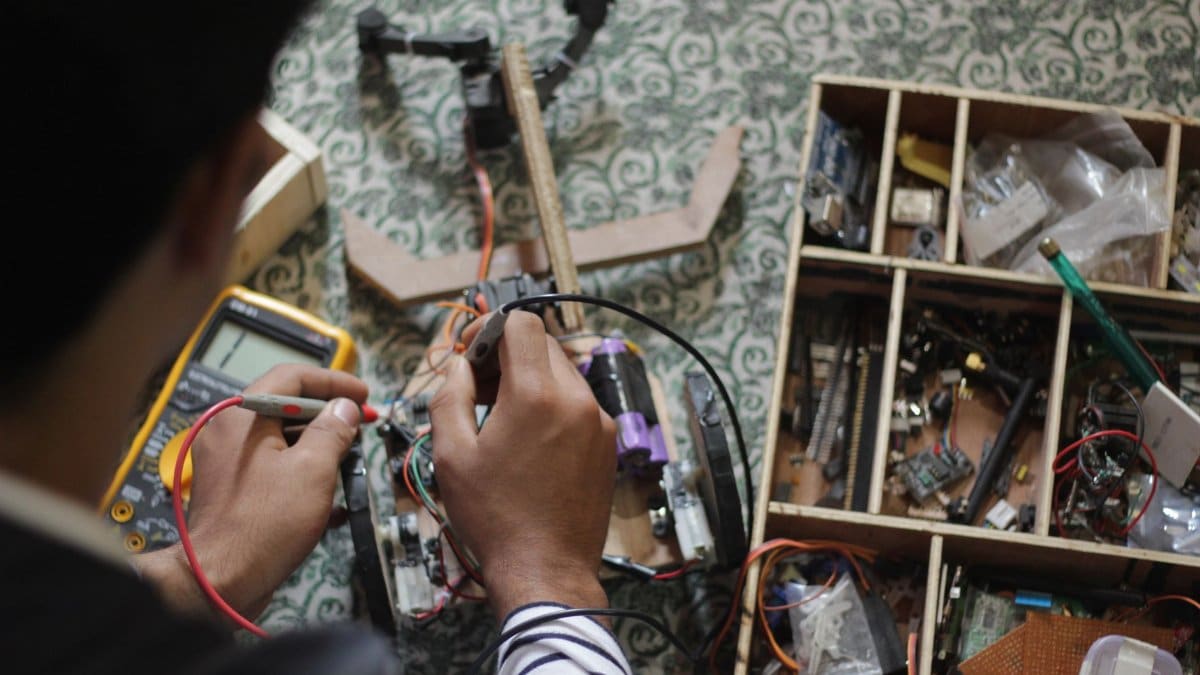 Man soldering electronic parts at a table filled with tools and equipment.