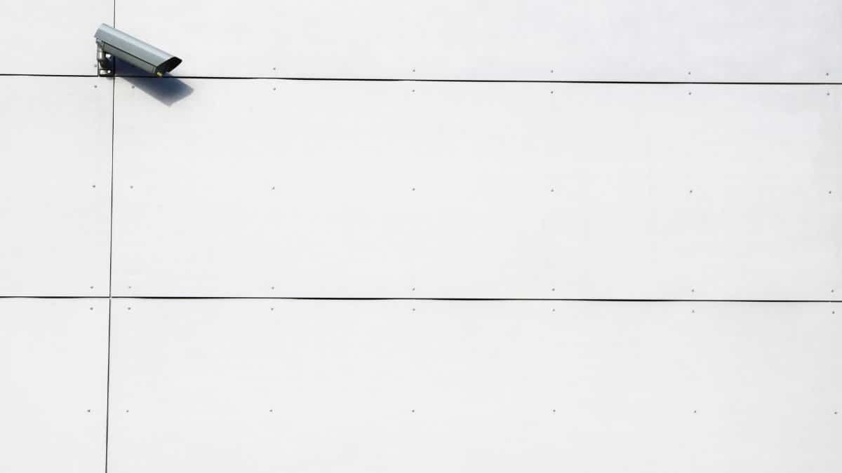 A minimalist image showcasing a single surveillance camera mounted on a stark white wall.