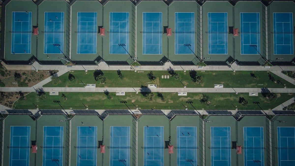 Drone view showcasing aligned tennis courts with clear pathways and greenery.