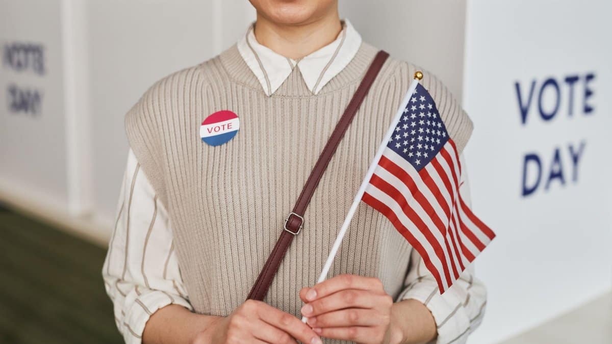 A woman proudly holds the American flag and smiles, celebrating voting day.