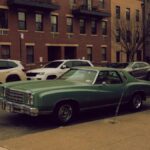 A classic Chevrolet muscle car parked on a city street amidst urban architecture.
