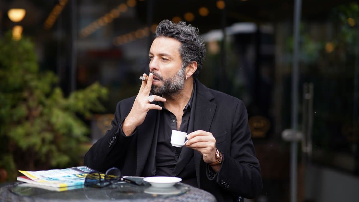 A contemplative middle-aged man enjoys coffee and a cigarette at an outdoor café.
