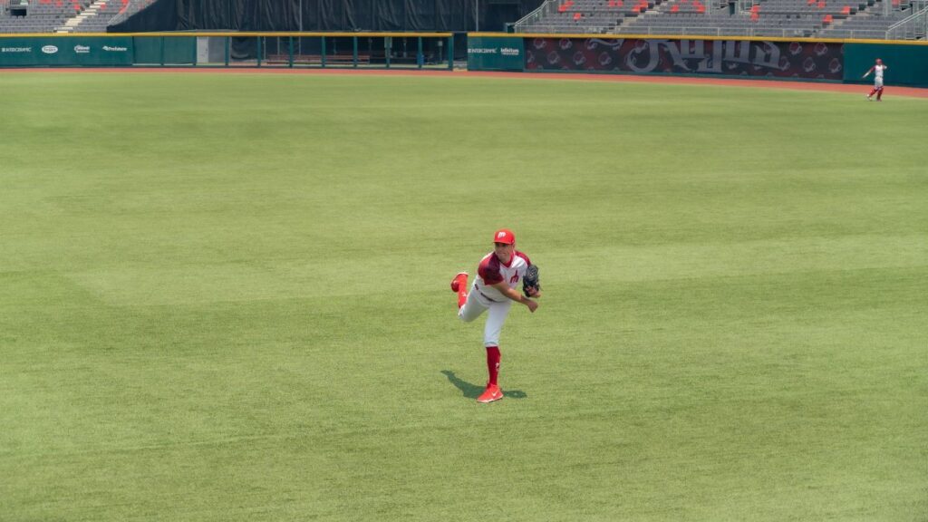 A baseball player pitching on a grass field in an empty stadium.