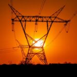 A striking sunset with electric power lines silhouetted against an orange sky in a vast open field.