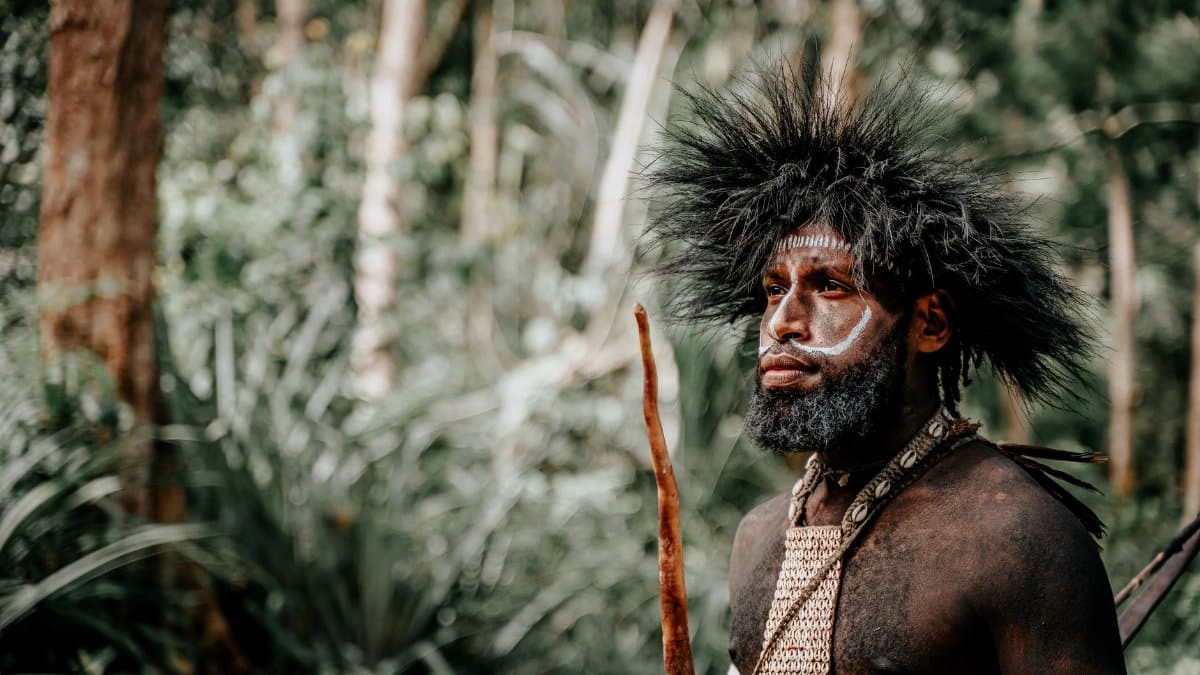 Portrait of an indigenous man with face paint and headdress in a lush jungle setting.