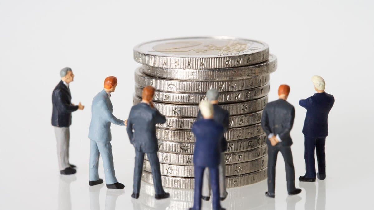 Miniature figurines of businessmen surround a stacked pile of coins on a clean white background.