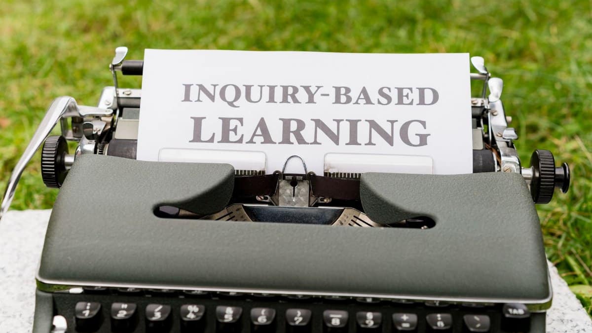 Close-up of a vintage typewriter with paper labeled 'Inquiry-Based Learning' outdoors.